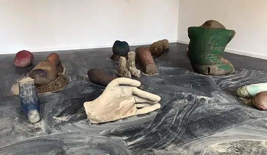 På ett mörkgrått golv står skulpturer av olika kroppsdelar utplacerade.