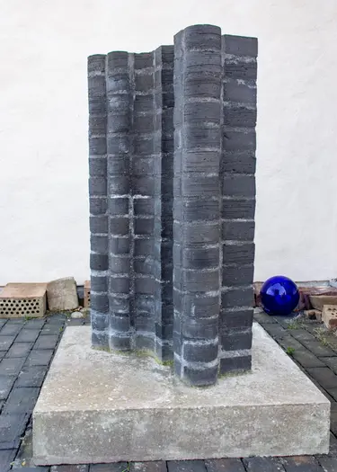 Ett konstverk, en skulptur av mörkgrått tegel står på ett betongfundament.