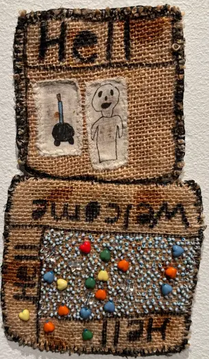 Broderad säckväv med applikationer, pärlor och skriven text på.